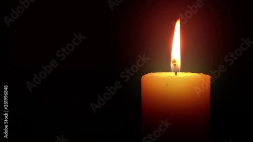 Illuminated Candle Loop is a stock video with a lit flame that flickers and glows in a dark environment. The wax is white or light yellow.