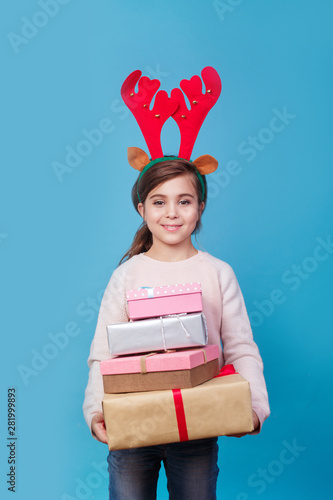 Smiling funny child with reindeer antlers holding Christmas gifts in hand. Christmas concept.