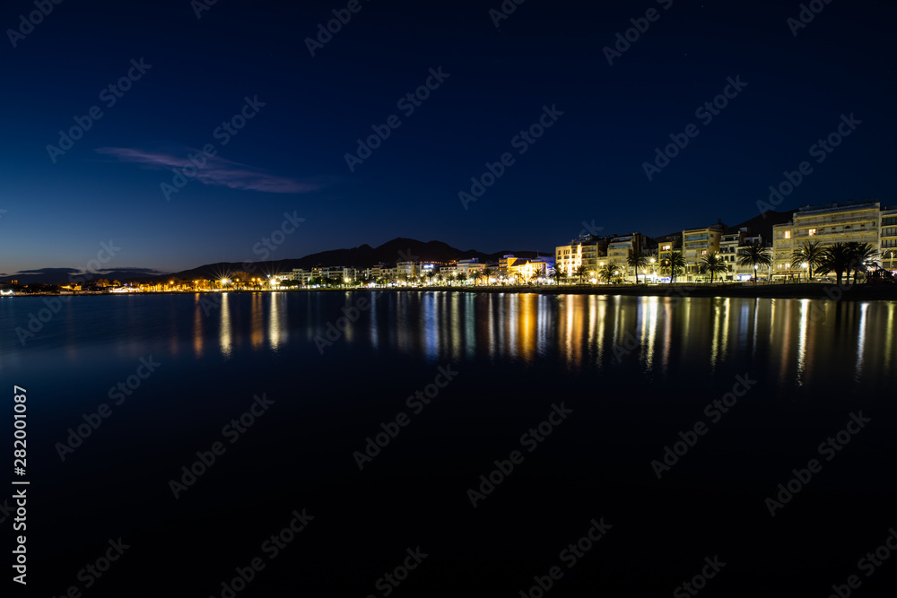 Long exposure of a coastline at night over the sea with city lights