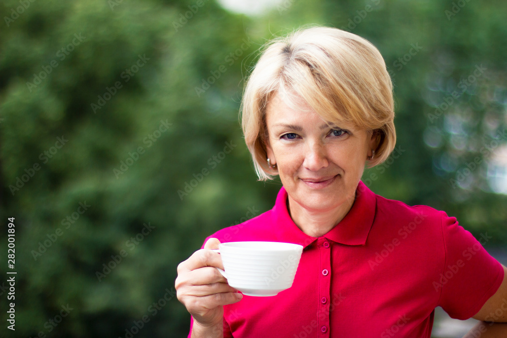 Portrait of a happy elderly adult woman looking at the camera, smiling with a cup of tea or coffee. Senior mature female pensioner drinking a drink outdoor in a summer day. Happy retirement concept Portrait of a happy elderly adult woman looking at the camera, smiling with a cup of tea or coffee. Senior mature female pensioner drinking a drink outdoor in a summer day. Happy retirement concept