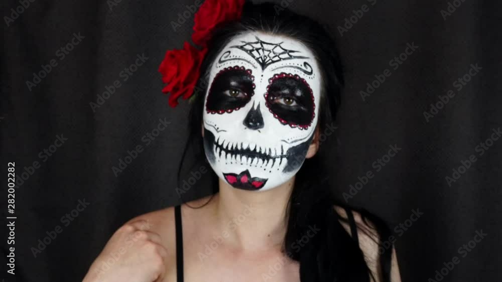 Halloween mask Catrina. Mexican day of the dead. Portrait of a young woman with scary makeup for Halloween on a dark background. 4K Halloween mask Catrina. Mexican day of the dead. Portrait of a young woman with scary makeup for Halloween on a dark background. 4K