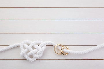Heart shaped rope and a double gold ring on white wooden background