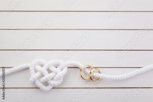 Heart shaped rope and a double gold ring on white wooden background