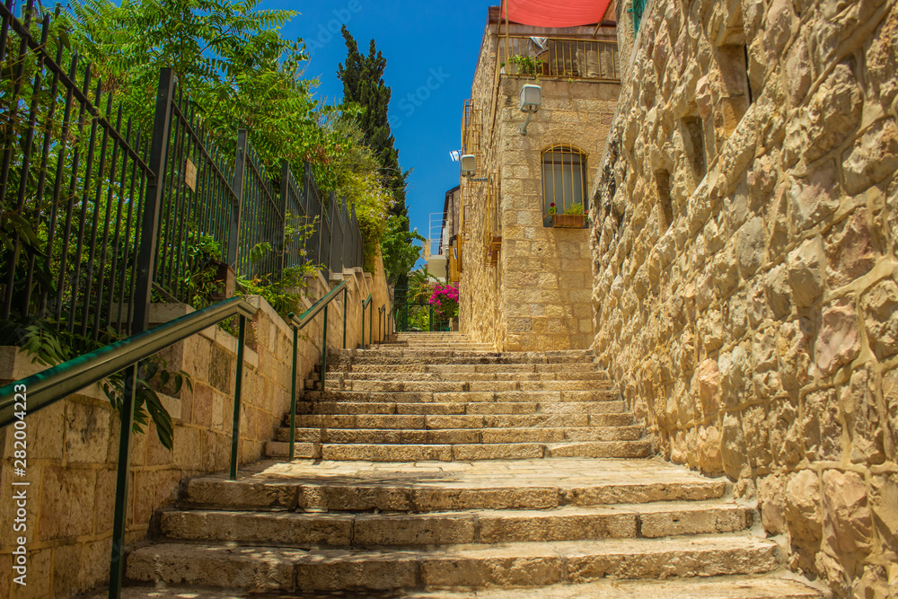 Jerusalem old city stone building landmark photography of stairway between street with monolithisch houses and garden fence in summr sunny colorful and bright clear weather time  