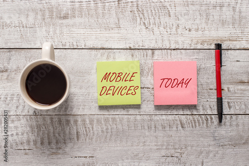 Word writing text Mobile Devices. Business photo showcasing A portable computing device like smartphone tablet computer Stationary placed next to a cup of black coffee above the wooden table photo