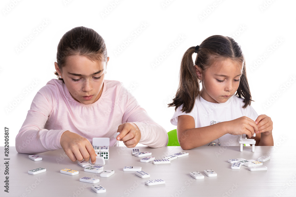 Two young girls of different ages playing with dominoes, concept of teamwork or unjust competition Two young girls of different ages playing with dominoes, concept of teamwork or unjust competition