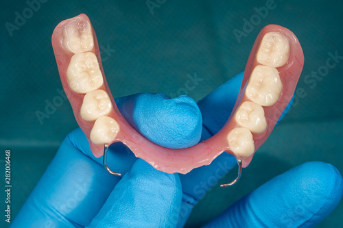 Close-up human denture of the upper jaw on a blue background in the hand of dentist wearing a medical a glove photo