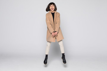 Charming young woman wearing a coat jump isolated over white background.