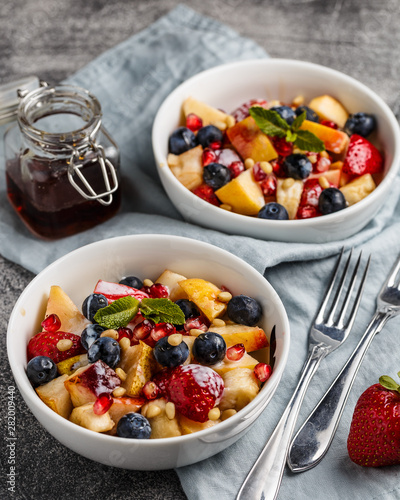 Fruit salad with apples, bananas, strawberries, blueberries, pomegranate seeds, pine nuts, yogurt and honey