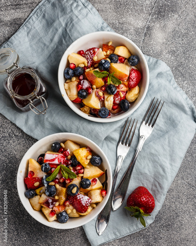 Fruit salad with apples, bananas, strawberries, blueberries, pomegranate seeds, pine nuts, yogurt and honey