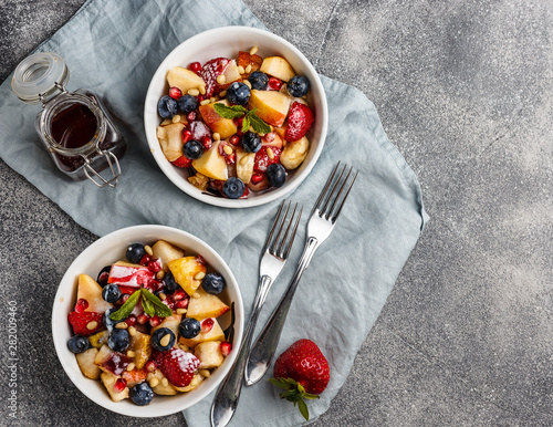 Fruit salad with apples, bananas, strawberries, blueberries, pomegranate seeds, pine nuts, yogurt and honey
