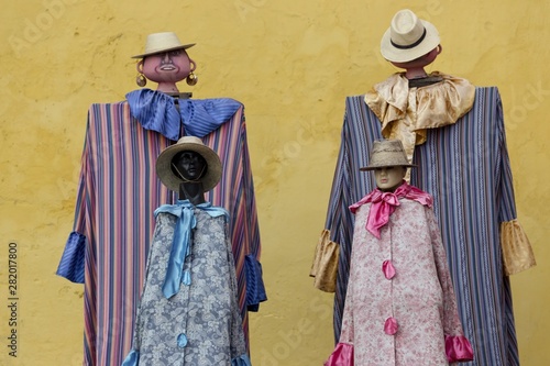 Human Dolls with tailored Guatemalan costumes in front Yellow Wall of Iglesia De La Merced Catholic Church in Old Town Antigua Guatemala