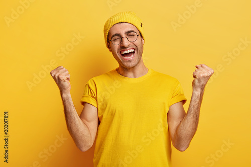 Photos Successful happy young male clenches fists in victory gesture, receieves champio
