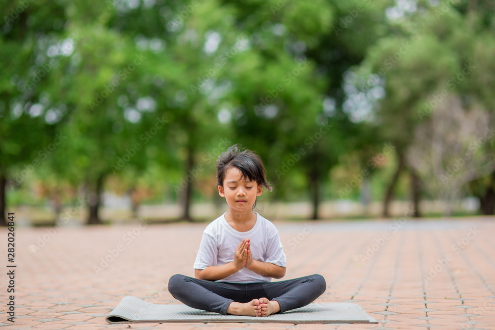 Fototapeta premium Little cute asian girl practicing yoga pose on a mat in park, Healthy and exercise concept