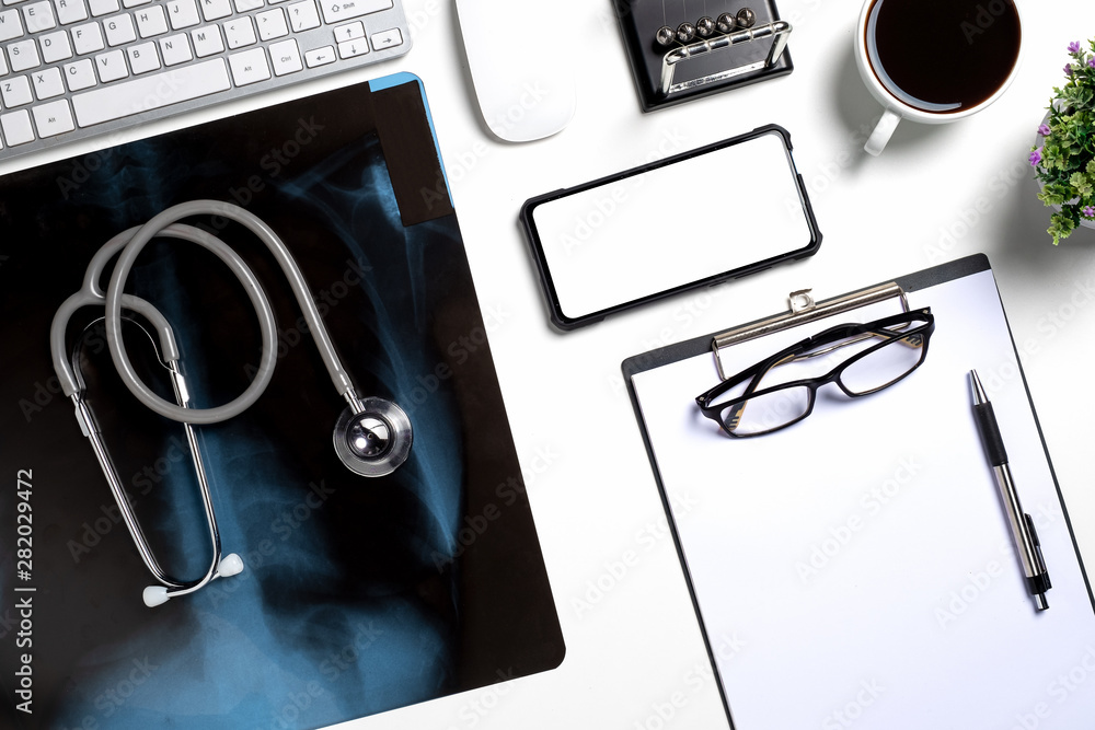 Top view of doctors desktop with stethoscope, glass, blank screen smart phone, mouse, keyboard and Xray film. - obrazy, fototapety, plakaty 