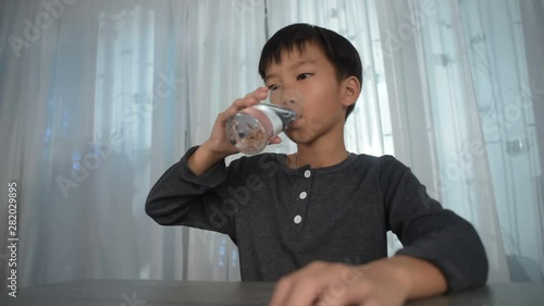 Low agle shot of slow motion young Asian boy drink water from a glass photo