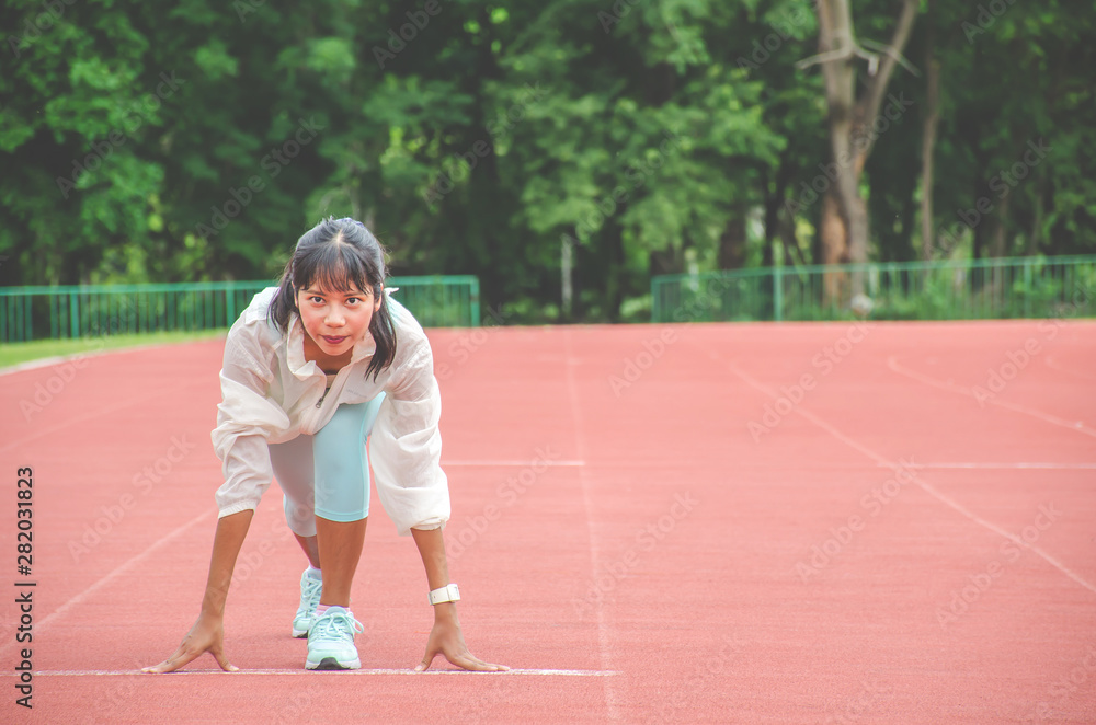 Young woman wearing sports clothes and ready to start running on the track in stadium, sport women