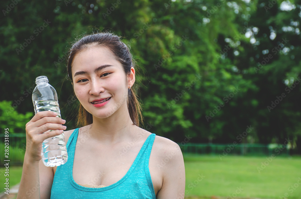 Shot of beautiful female runner standing outdoors holding water bottle. Fitness woman taking a break after running workout.. Shot of beautiful female runner standing outdoors holding water bottle. Fitness woman taking a break after running workout..