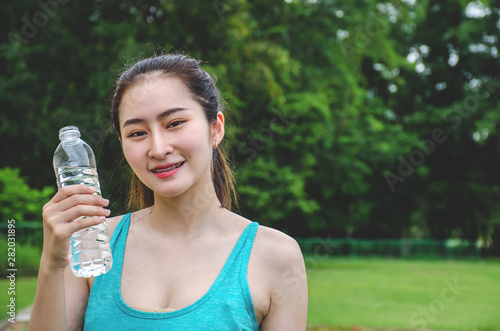 Shot of beautiful female runner standing outdoors holding water bottle. Fitness woman taking a break after running workout..