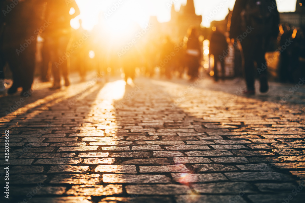 Busy European street at the sunset. People are blurred with a lens. Old pavement. - obrazy, fototapety, plakaty 
