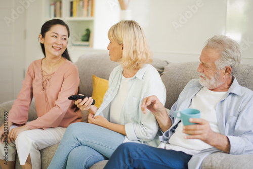 Group of positive seniors European and Asia are sitting on the big sofa and talking which looking television at retirement home. Retired old people are smiling and felling happy. © linghaa