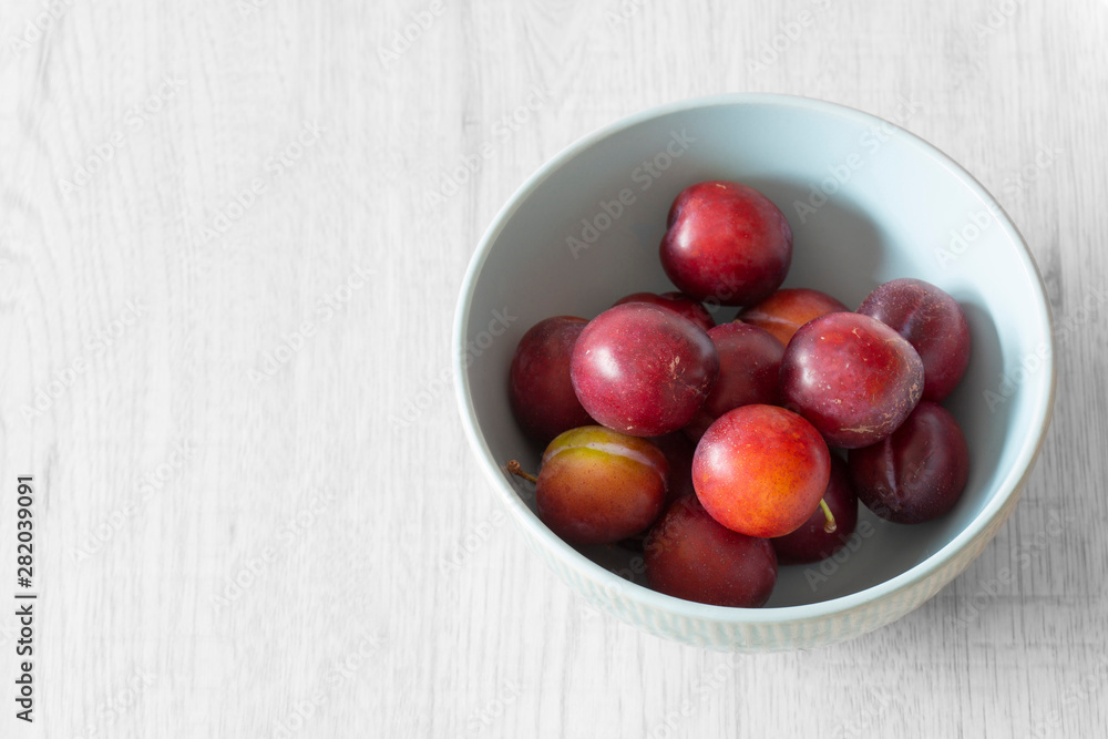 British organic plums, freshly picked, in a pastel green bowl dish. Grey wood background British organic plums, freshly picked, in a pastel green bowl dish. Grey wood background