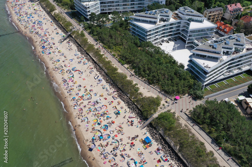 Drone aerial perspective view on sunny beach with sunbathers with windbreaks and towels at sea in touristic city