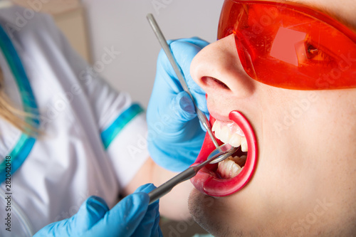Dentistry. Examination of teeth with the help of a dental mirror close-up. A young man is a patient with an open mouth and Protective goggles.