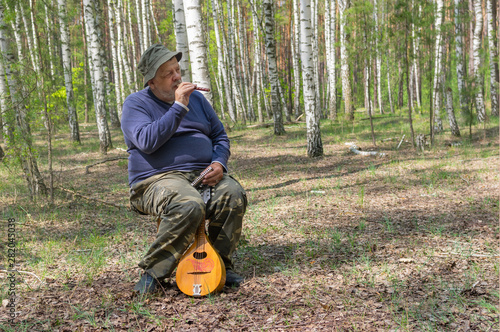 Seniors playing music on woodwind instrument sopilka while sitting on a stool in birch forest photo