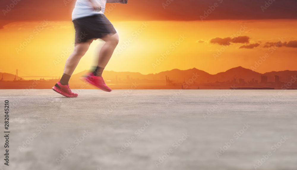 Healthy lifestyle and losing weight. Young man running on concrete road in summer sunset