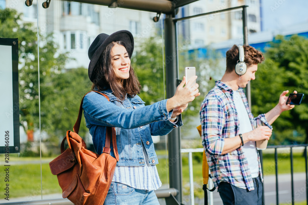 Happy european traveler couple bloggers man and woman strangers taking selfie with smartphones at tram stop during summer vacation trip adventure.