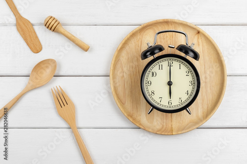 Top view of a wooden dish and eating utensils with a clock