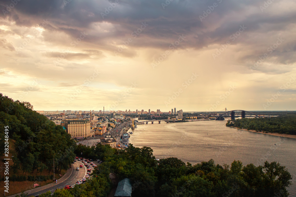 View from above to the Kyiv city and Dnipro river, Ukraine. cloudy sky before rain with warm sunset light
