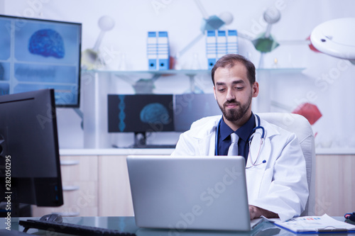 Serious doctor typing a treatment on his laptop