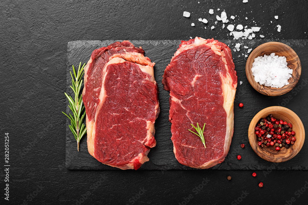 Raw meat, beef steak with spices on black background, top view.