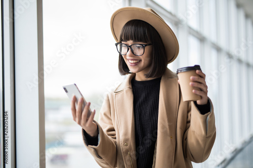 Young pretty business woman use smartphone with cooffe in office by window photo