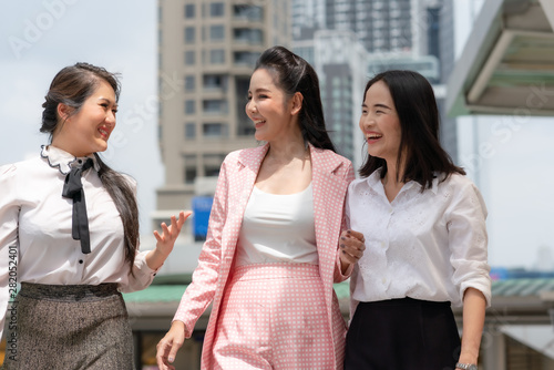 Happly asian businesswoman talking and smilling with colleagues while walking on city street