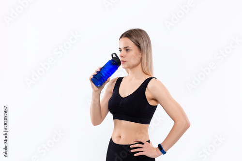 Young sporty blond woman in a black sportswear with smart watches drinks water after workout standing over white background. © ianachyrva