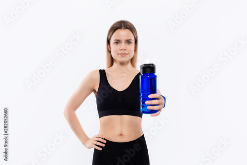 Young sporty blond woman in a black sportswear with smart watches holds bottle with water after workout standing over white background. © ianachyrva