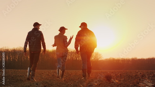 Three farmers go ahead on a plowed field at sunset. Young team of farmers