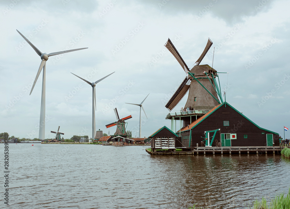 Collage of Netherlands old village Zaanse Schans with old wind mills and modern wind mills (Wind generators) in cloudy day. Contrast between old and new era, century. Spring of 2019 year