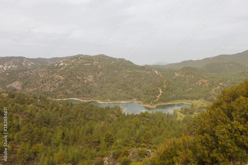 Beautiful landscape with mountains and lake. Turquoise water and beautiful winding shores with coniferous forests against the cloudy sky. Cyprus