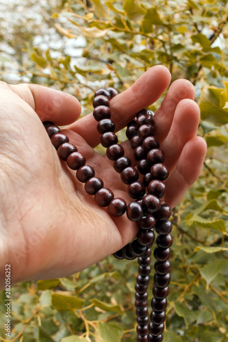 a yogi holds rosary of sandalwood yoga beads, blurred summer forest in a background. prayer Wooden rosary beads for the spiritual practice in a hand, selective focus, vertical image.