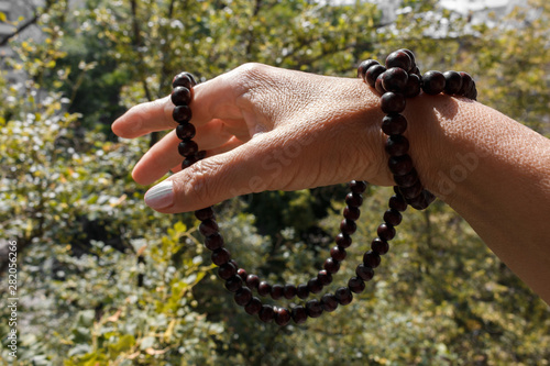 wooden rosary beads wound on the hand of a religious woman. mahogany rosary wrapped around fingers, selective focus, blurred trees in a background. Praying with rosary, hand holding rosary. photo