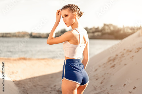 Beautiful athletic girl stands with her back near the lake after morning exercise. Back view of elastic female buttocks © Andrii