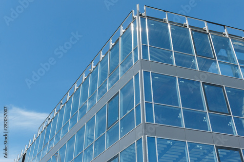 the corner of the modern building  which consists of a metal frame and transparent glass windows. glass wall of new office building with sky reflection. Windows reflect clear blue sky.