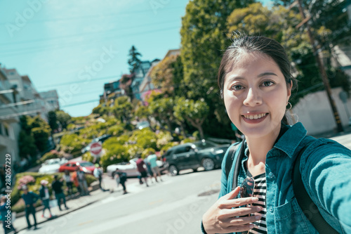 young girl tourist face camera smiling taking selfie while sightseeing in lombard street in San Francisco United State. woman traveler make self photo on sunny day in famous attraction outdoors.