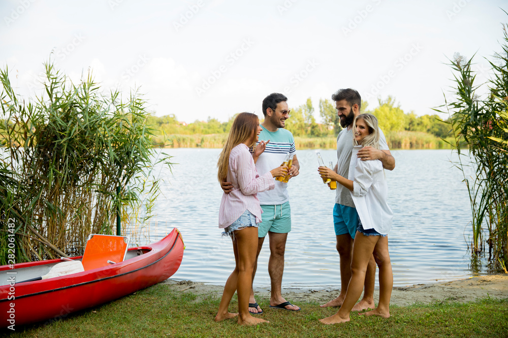 Obraz premium Group of friends with cider bottles standing by the boat near the beautiful lake and having fun
