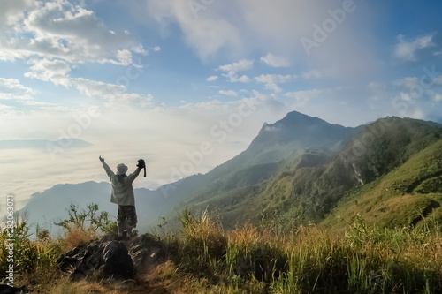 Mountain view morning of a photographer standing on top hill around with soft mist and cloudy sky background  sunrise at Pha Tang  Chiang Rai  northern of Thailand.
