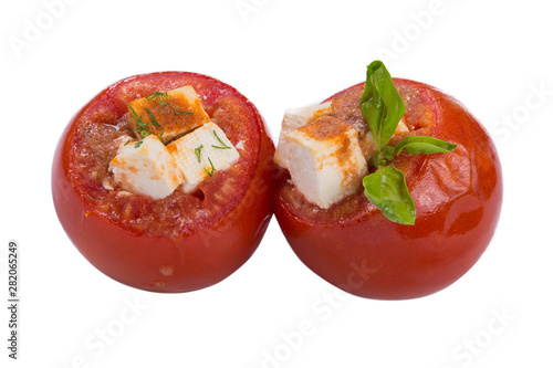 two baked stuffed tomatoes with feta cubes and with herbs, on a white background